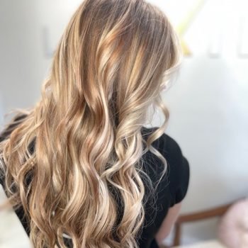 A woman with long blonde hair styled with Loxxie hair products, showcasing a sleek and polished look.