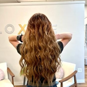 A woman with Loxxie long wavy hair in a red plaid shirt, posing confidently for the photo.