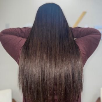 A woman with long wavy Loxxie hair wearing a red plaid shirt, smiling at the camera.