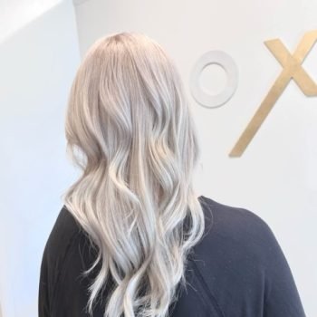 A woman with long blonde hair styled with Loxxie hair products poses for the camera, showcasing her vibrant hairstyle.