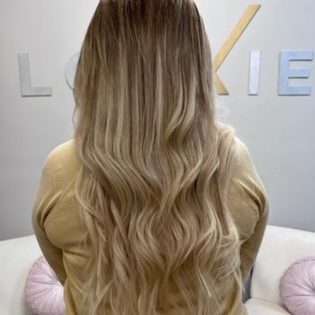 A woman displays her long blonde hair, enhanced by Loxxie hair products, radiating shine and elegance.