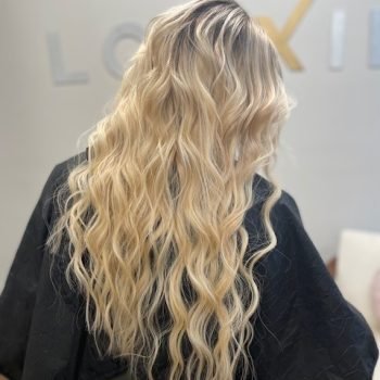 A woman with flowing blonde hair, featuring Loxxie hair products, is captured in a stylish photo.