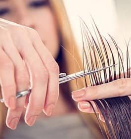 A woman is using scissors to cut another woman's hair at Loxxie Hair salon.