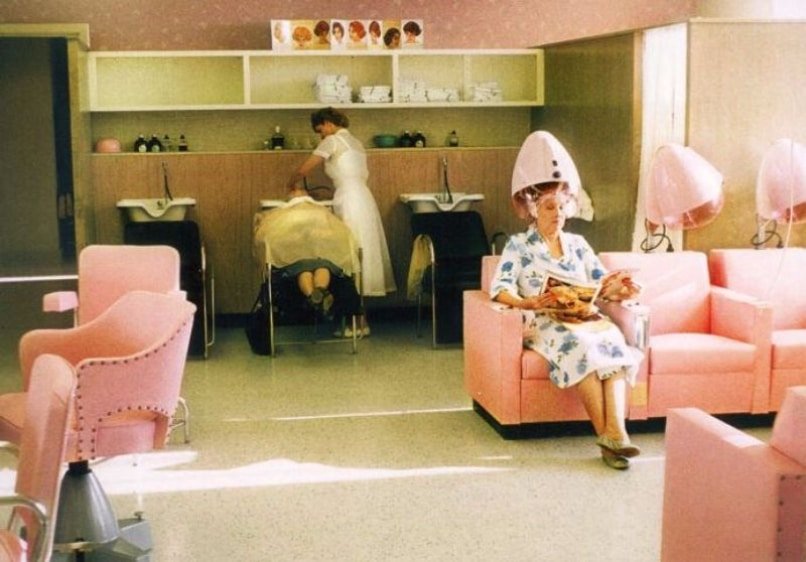 A woman enjoys her time in a pink salon chair at Loxxie Hair, accompanied by a small dog on her lap.