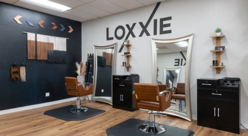 Loxxie Hair salon is adorned with sleek black walls and polished wooden floors, offering a chic and welcoming environment.