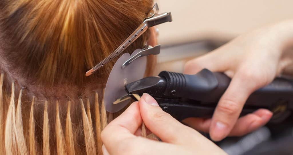 A woman is cutting another woman's hair with scissors at Loxxie Hair salon.