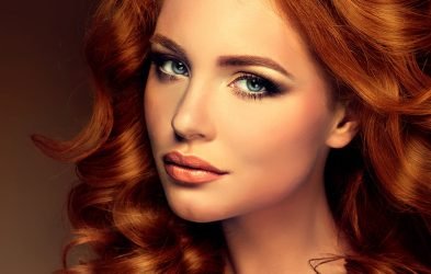 Beautiful redhead woman with long, curly hair, showcasing Loxxie Hair products in a vibrant setting.