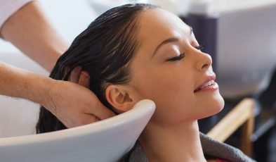 A woman relaxes as her hair is washed at Loxxie Hair salon, with water cascading over her head in a serene setting.
