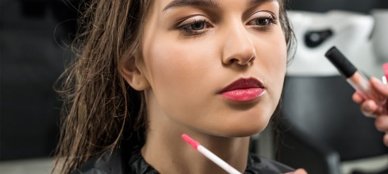A woman receives makeup application from a professional artist at Loxxie Hair studio.